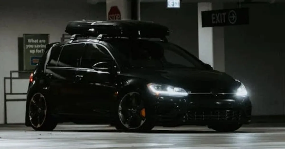A Black Car With Lights On Parked In An Underground Airport Parking Garage